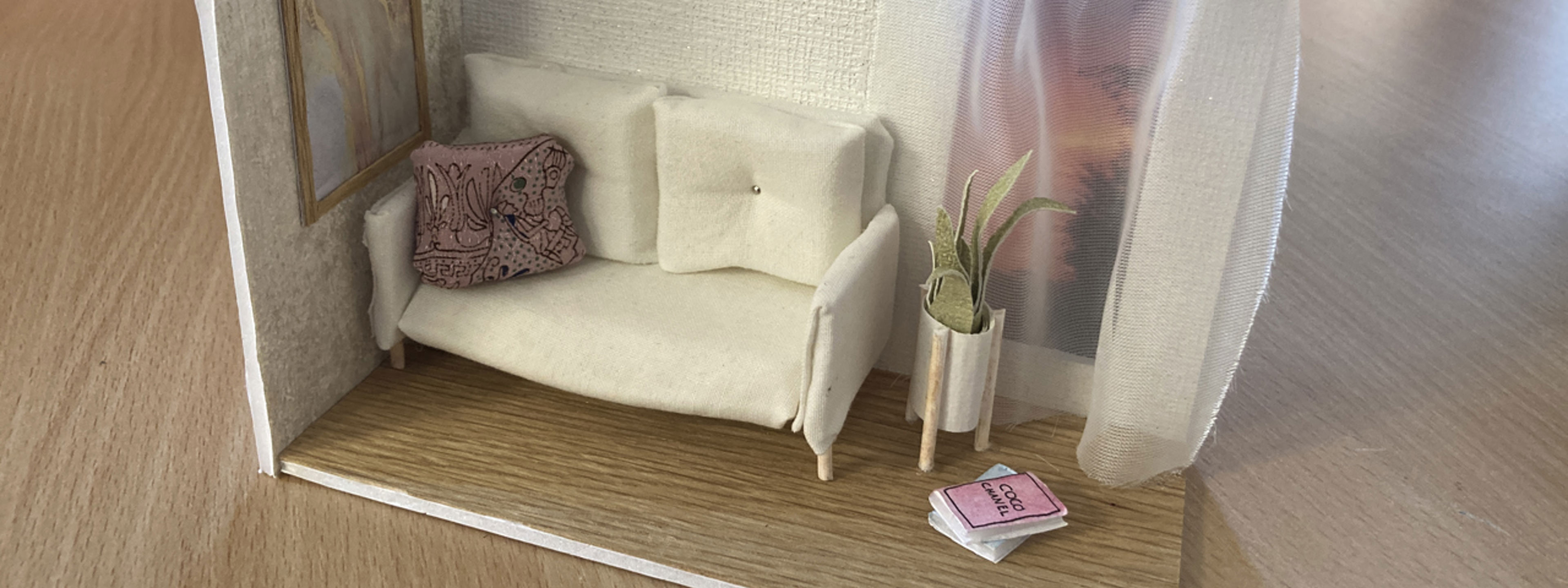 Ein modell i papp med sofa, blome og nokre bøker på gulv.