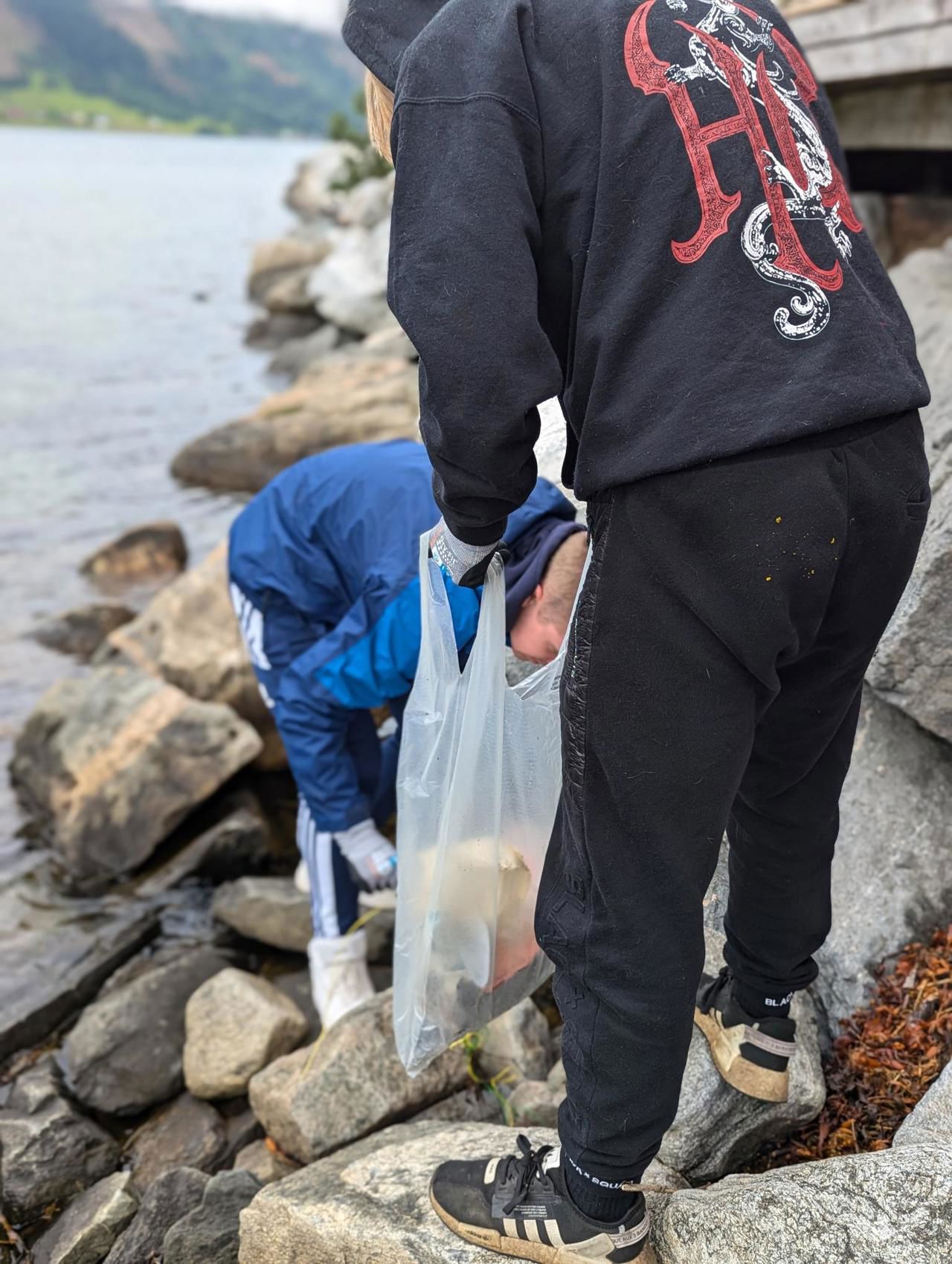 To elevar med ryggen til som plukkar plast i fjæresteinane.